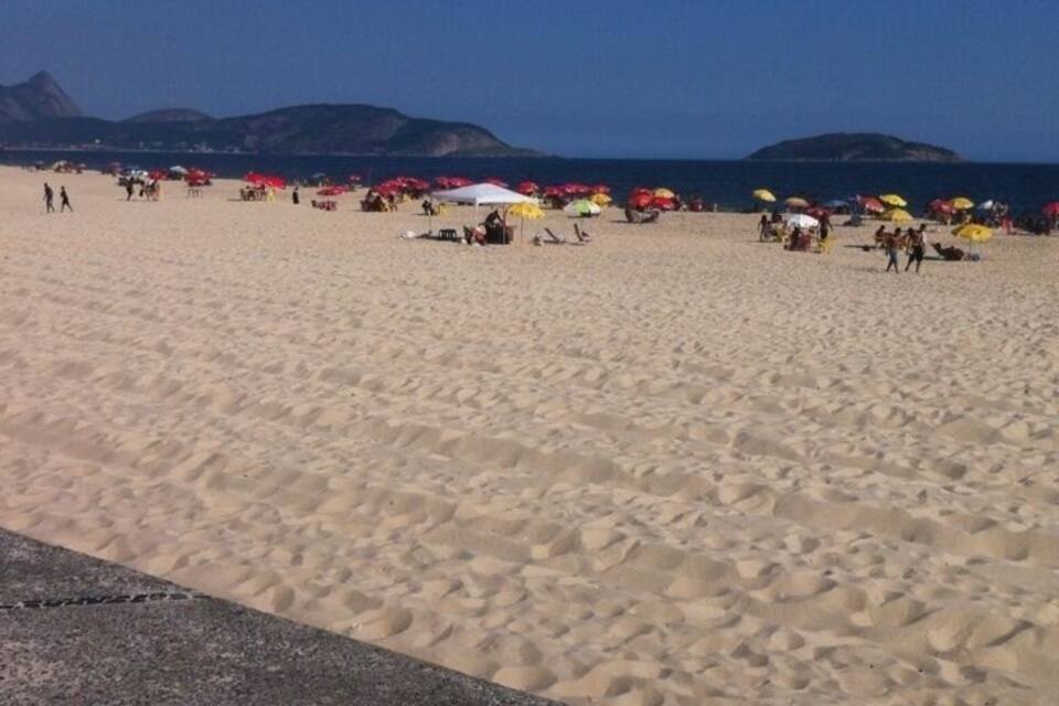 Uma praia com pessoas, guarda-sóis e montanhas ao fundo.