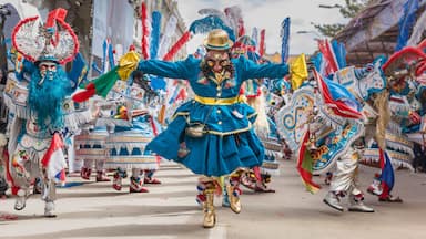 A person in a blue and gold costume with a large headdress, dancing in a parade.