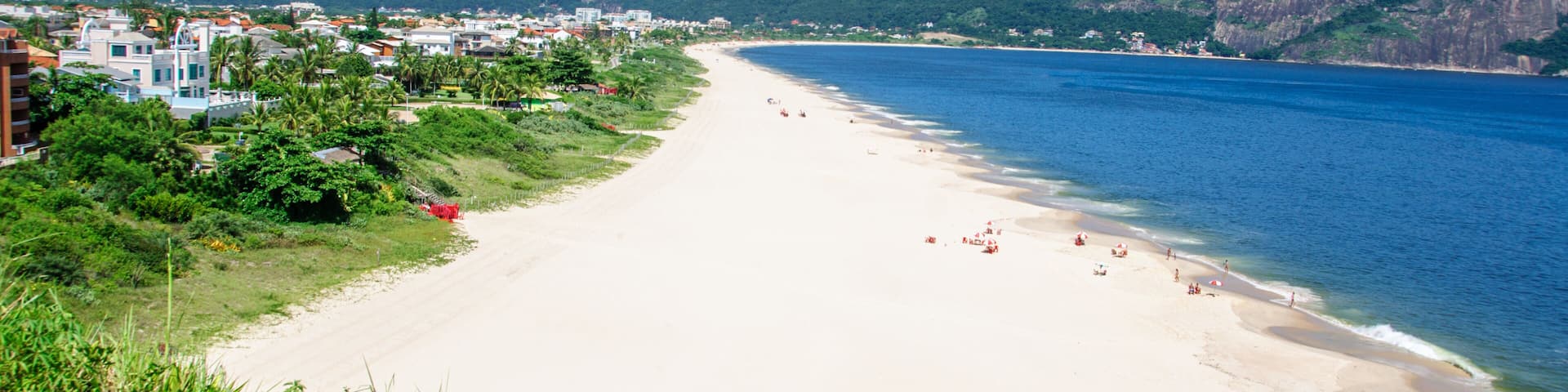 View of the beautiful Camboinhas Beach with houses, green trees, white sand, blue ocean and mountains on the background, Niteroi, Rio de Janeiro, Brazil