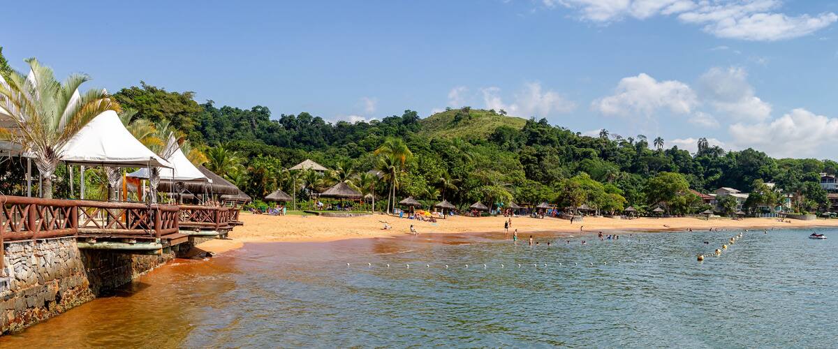 A beach with a wooden bridge, beach huts, and boats on the water.