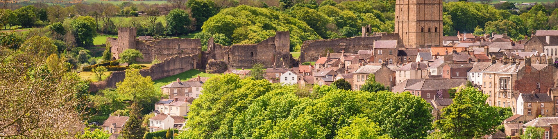 Uma cidade histórica com uma torre imponente, vegetação exuberante e colinas ao redor.