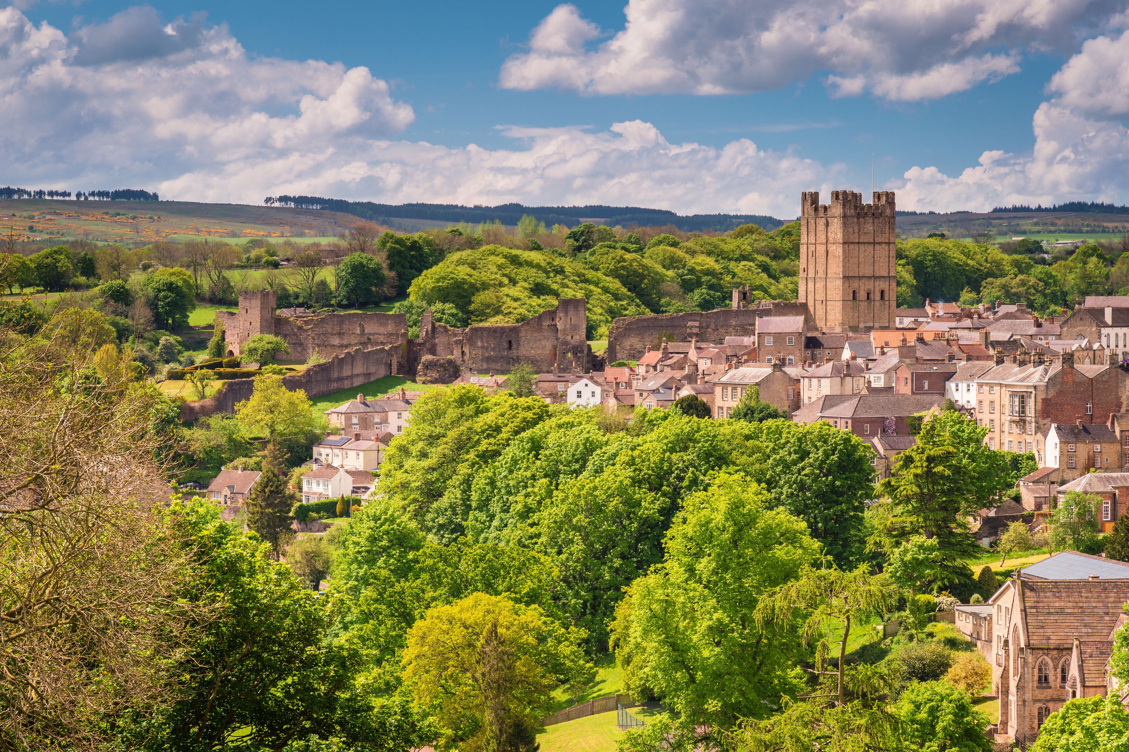 A historic town with a prominent tower, lush greenery, and surrounding hills.