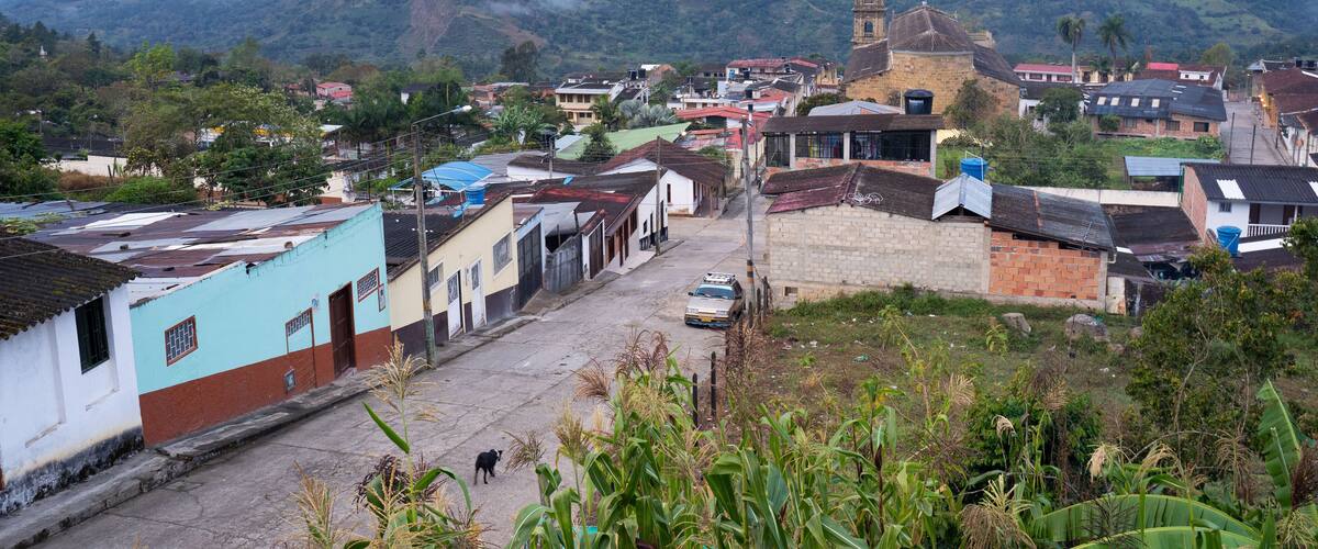 A town with a prominent church tower, a winding street, and lush green mountains in the background.