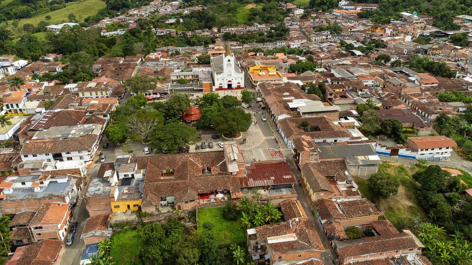 An aerial view of a densely populated town with terracotta-roofed buildings, a prominent church, and surrounding greenery.
