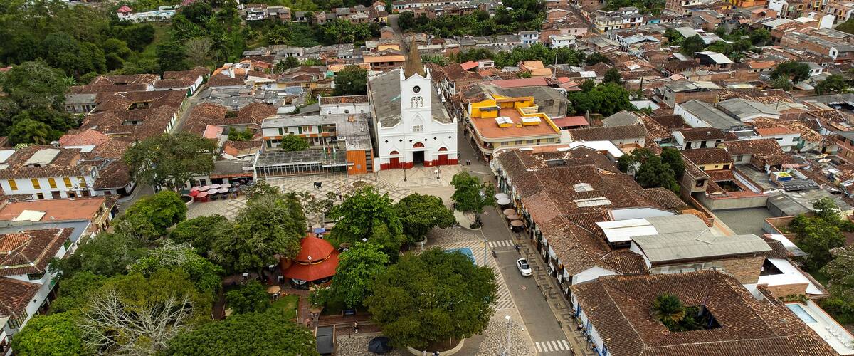 An aerial view of a town with a prominent church, a plaza with trees, and a mix of residential buildings.