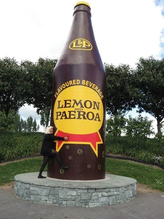 A large sculpture of a bottle labeled 'Lemon Paeroa' with a person leaning against it.