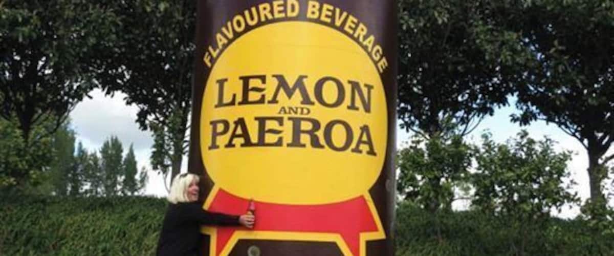 A large sculpture of a bottle labeled 'Lemon Paeroa' with a person leaning against it.