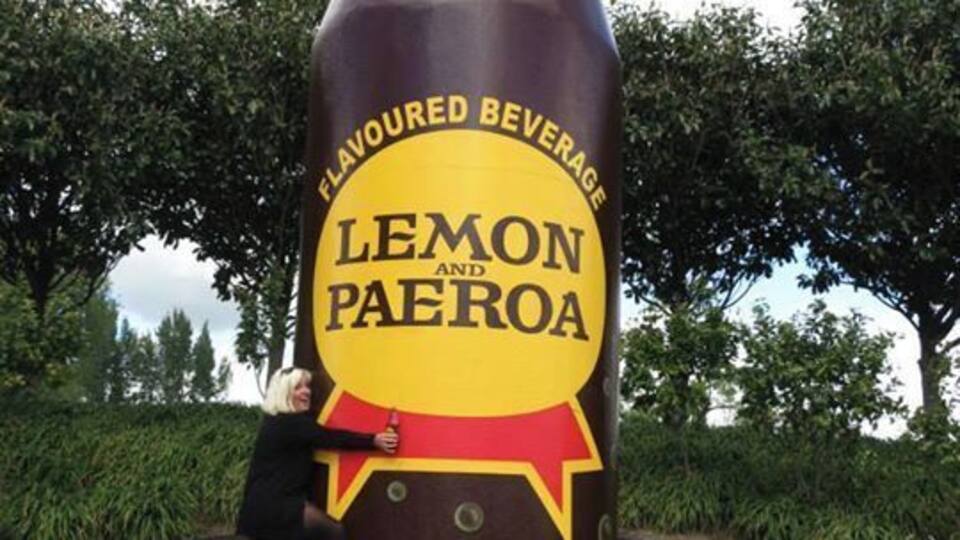 A large sculpture of a bottle labeled 'Lemon Paeroa' with a person leaning against it.
