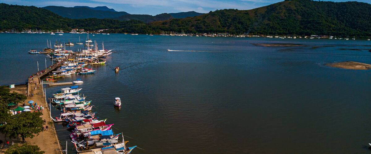A harbor with numerous colorful boats docked along the shore, surrounded by a mountainous landscape.