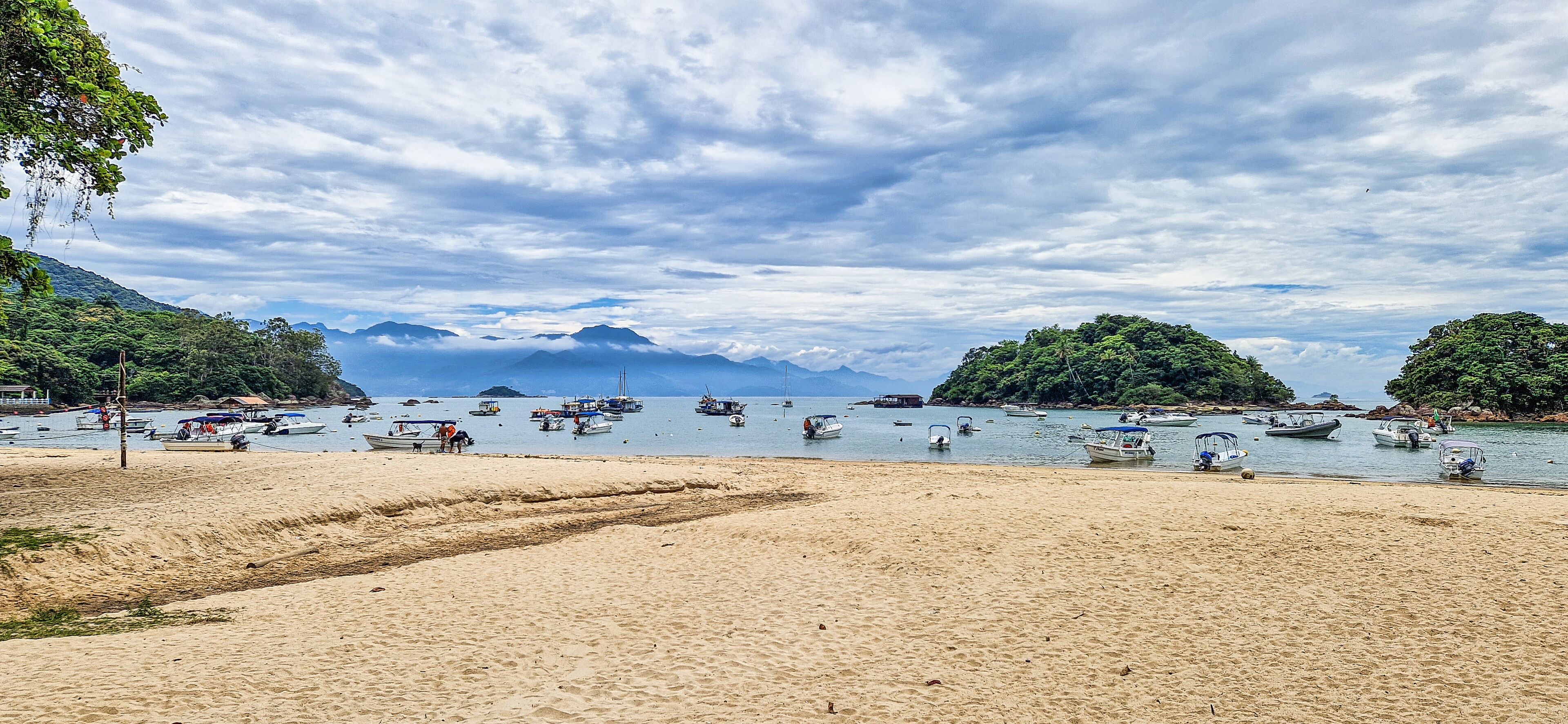 A beach with boats, mountains, and a cloudy sky.