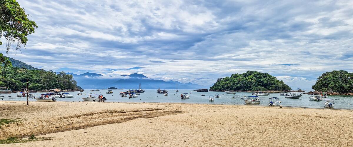 A beach with boats, mountains, and a cloudy sky.