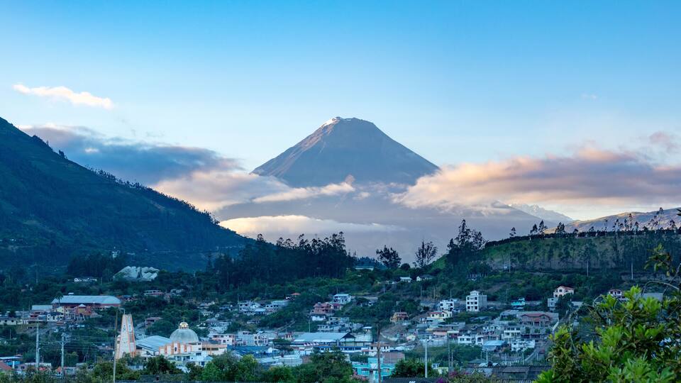 A mountain with a snow-capped peak, a town with buildings, and lush greenery.