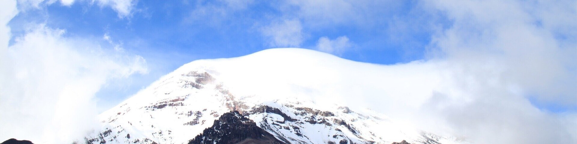 Una montaña nevada con un cielo azul despejado y un primer plano cubierto de hierba.