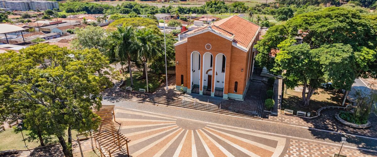 An aerial view of a church with a sunburst pavement design, surrounded by trees and fields.