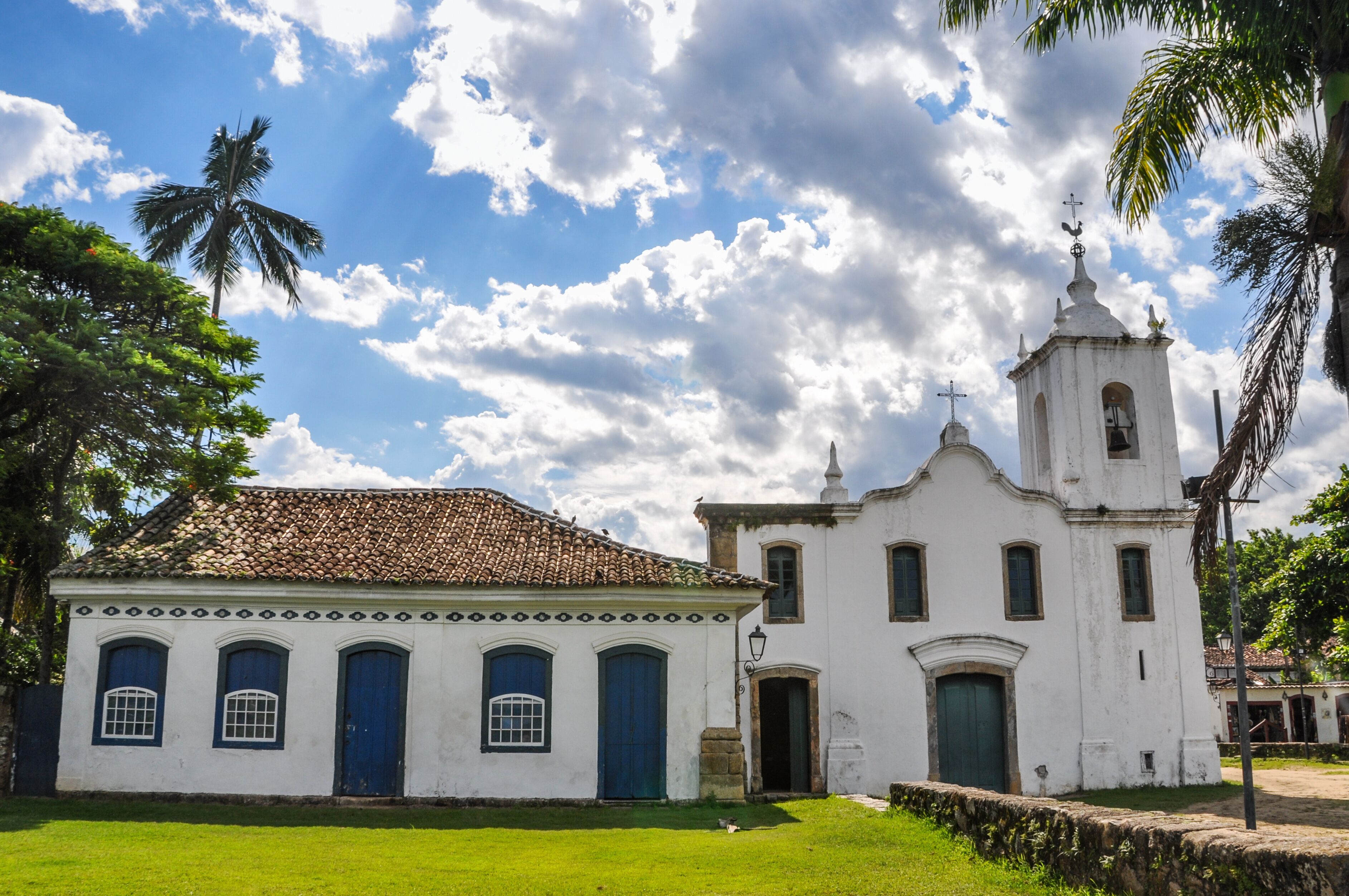 A white colonial-style building with a bell tower and a smaller adjacent building with blue doors.