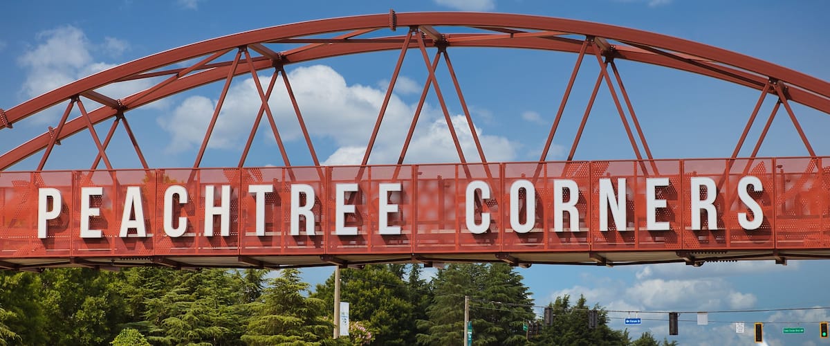 A large red arch sign with the words "PEACHTREE CORNERS" in white letters.