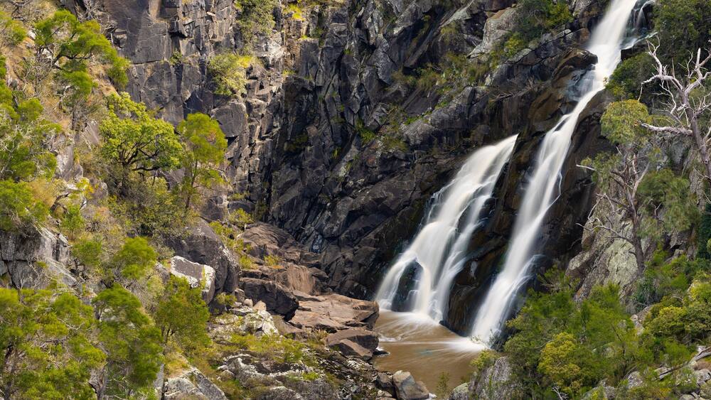 Une cascade d’eau se précipitant le long d’une falaise rocheuse, entourée d’un feuillage verdoyant.