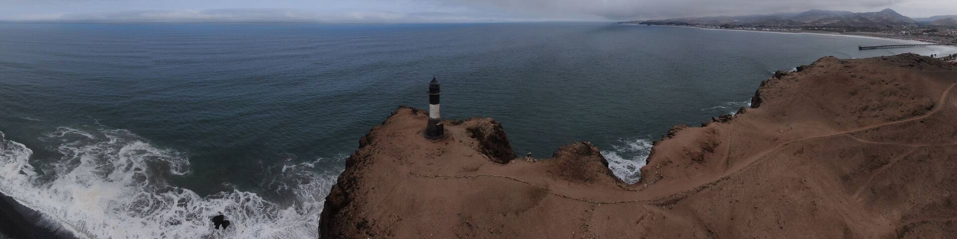A coastal landscape with a lighthouse on a rocky outcrop, a distant shoreline, and mountains in the background.
