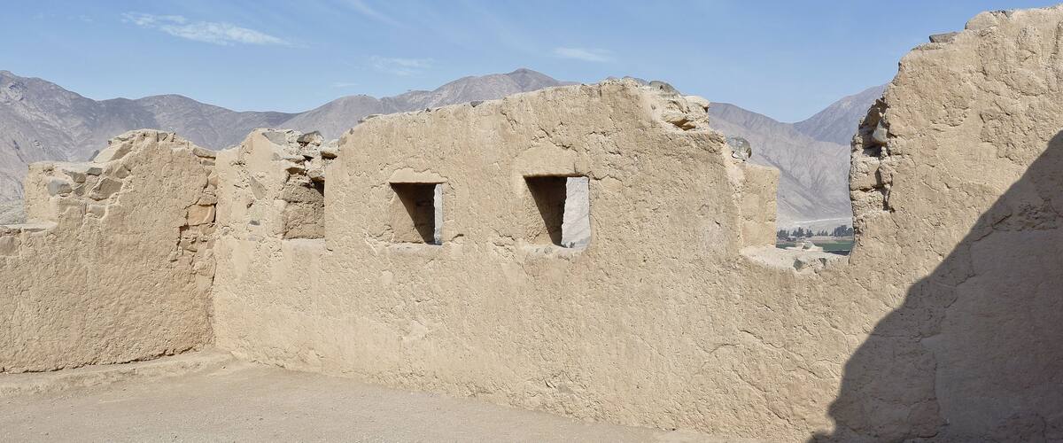 Ancient ruins with two small windows, set against a mountainous backdrop under a clear sky.