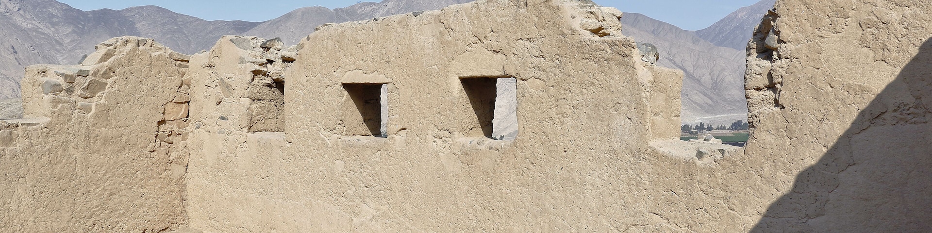 Ancient ruins with two small windows, set against a mountainous backdrop under a clear sky.