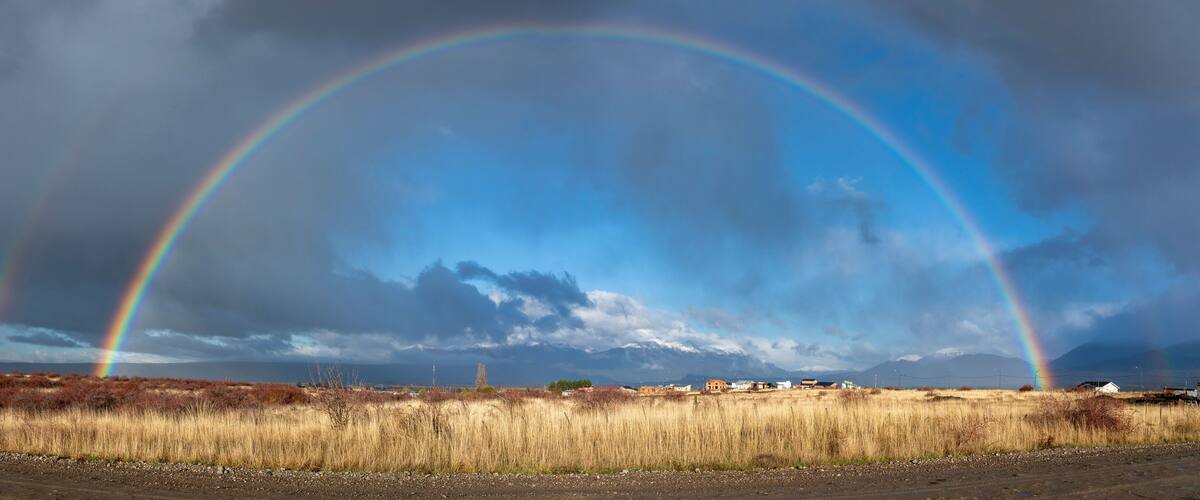 A landscape with two rainbows, a cloudy sky, and a distant mountain range.