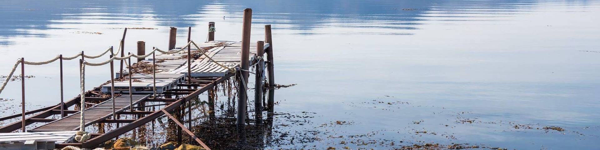 A wooden pier extending into a calm lake with mountains in the background.
