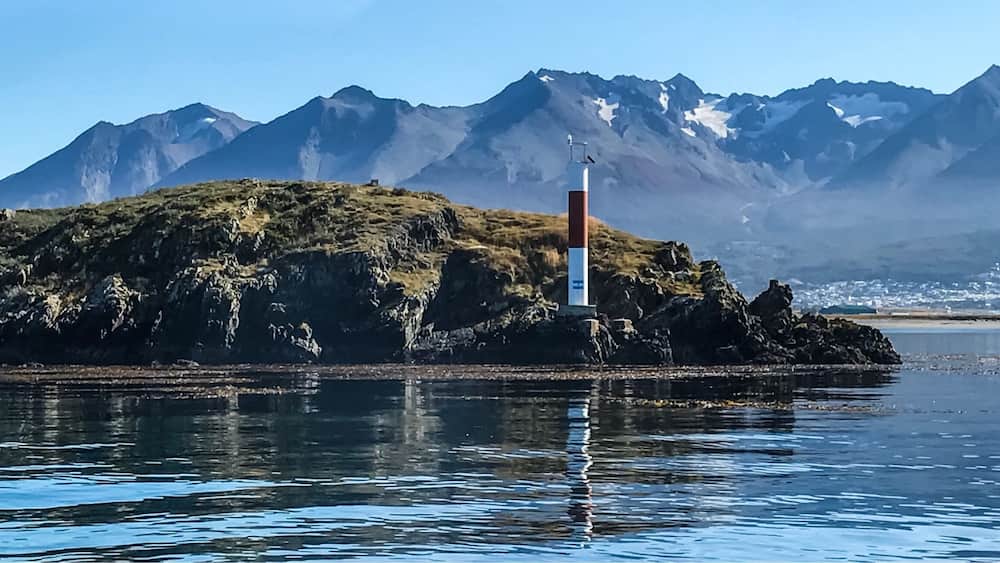 Un phare sur une île rocheuse, avec une chaîne de montagnes en arrière-plan.