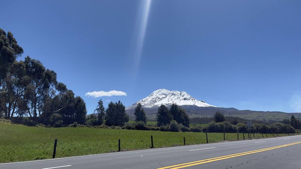 A snow-capped mountain, a clear blue sky, and a road with a fence.