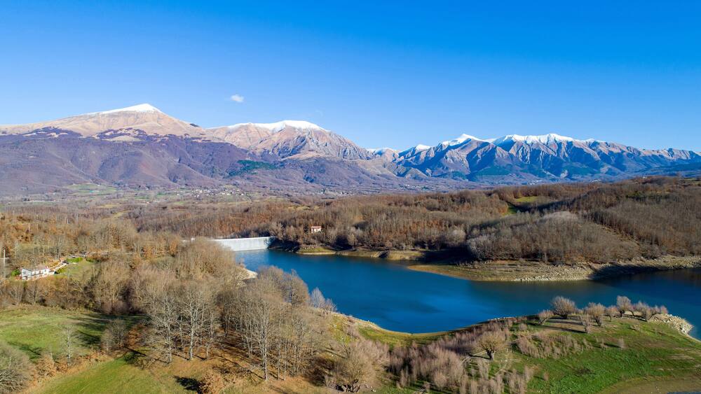 Aerial view of Scandello lake in Amatrice, Italy. Beautiful autumn landscape with lake, forest and mountains with snow-capped peaks in the background.