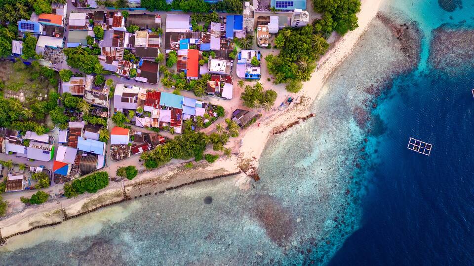 An aerial view of a coastal town with colorful buildings, a sandy beach, and clear blue waters.