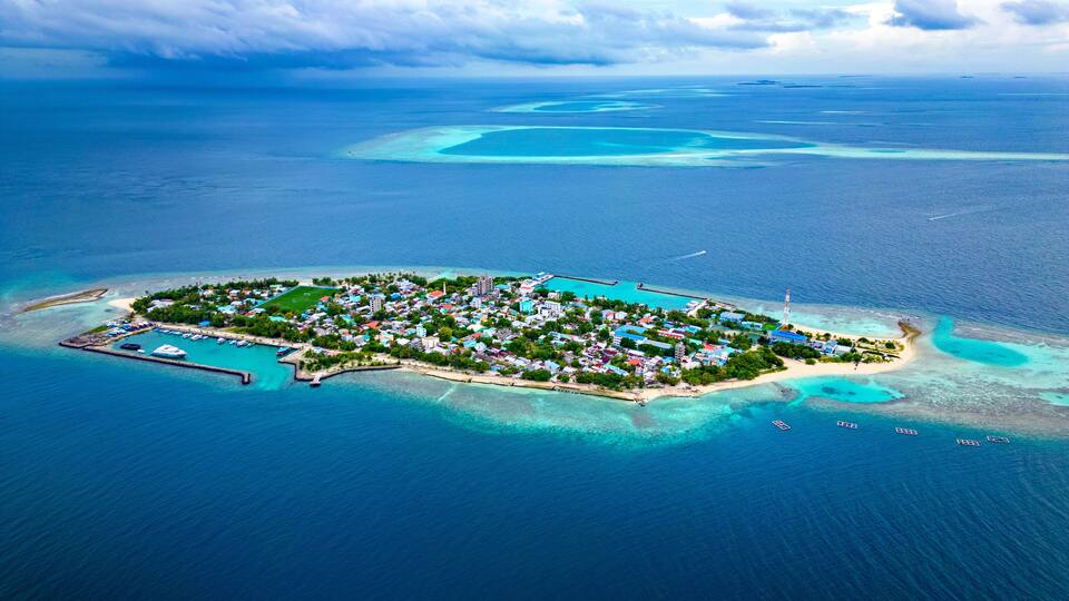 An aerial view of a tropical island with clear turquoise waters, a marina, and a mix of residential and commercial buildings.