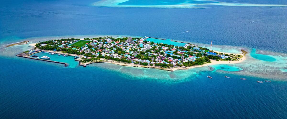 An aerial view of a tropical island with clear turquoise waters, a marina, and a mix of residential and commercial buildings.