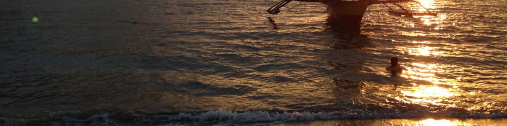 A boat anchored near a beach during sunset with mountains in the background.