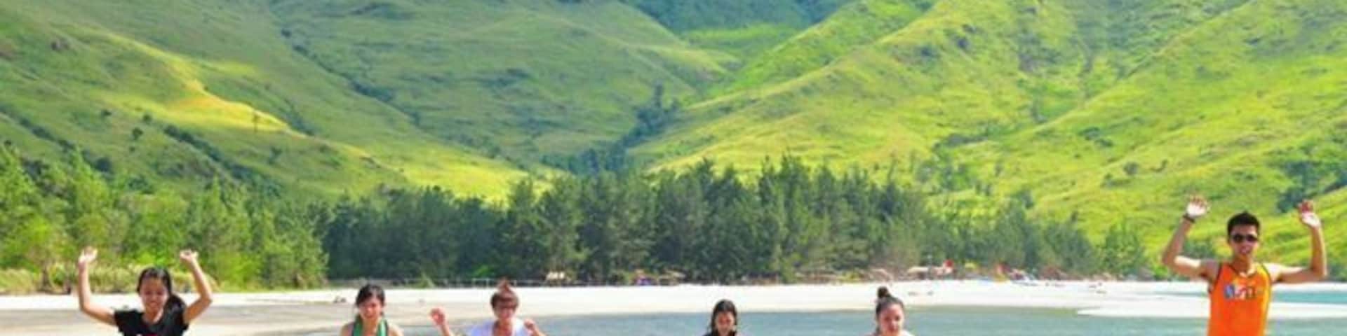 Un grupo de personas caminando en una playa con montañas al fondo.