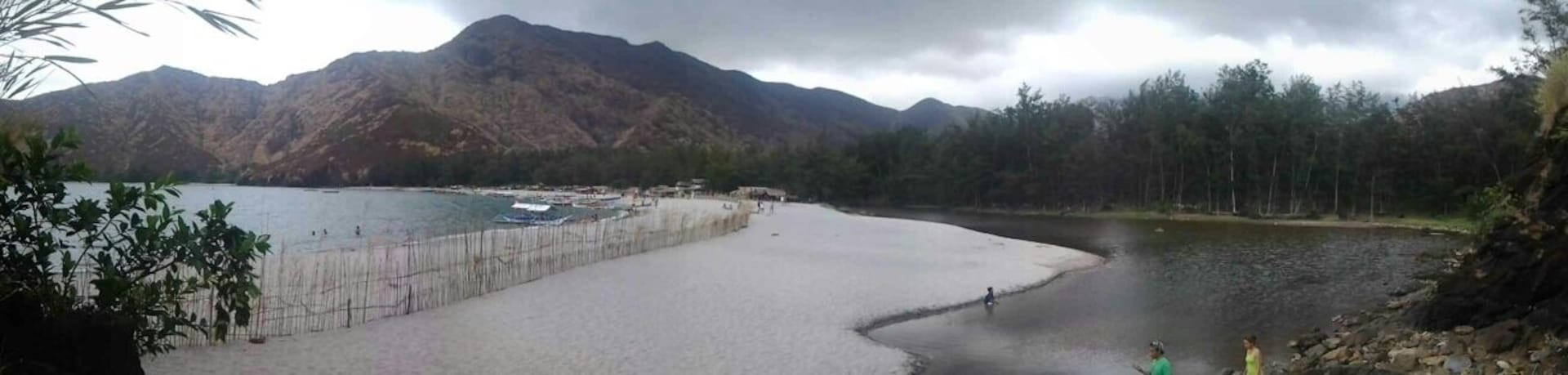 Ein See mit Bergen im Hintergrund, ein Sandstrand und einige Personen in der Nähe des Wassers.