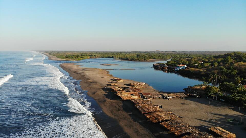 A coastal landscape with a beach, a river, and scattered buildings.