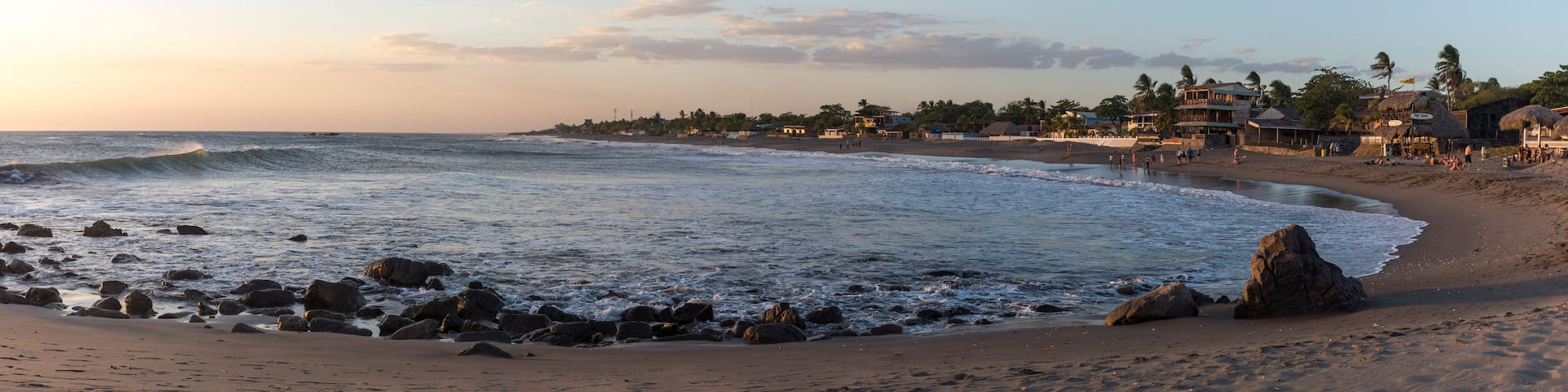 A beach with waves, rocks, and houses along the shore.