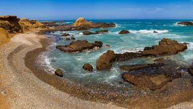 Litoral rochoso com águas turquesa cristalinas e grandes pedras.