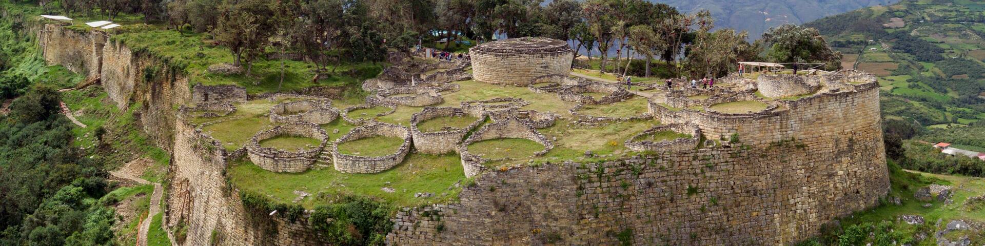 Ancient ruins on a hillside with a circular stone structure and a surrounding wall.