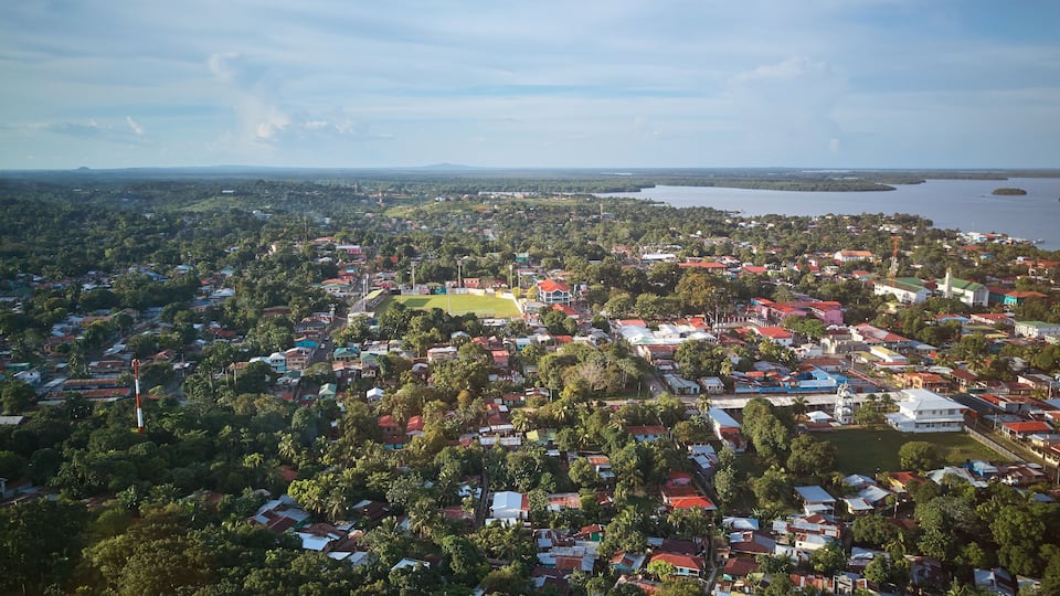 An aerial view of a coastal town with dense housing, a central green area, and a large body of water in the background.
