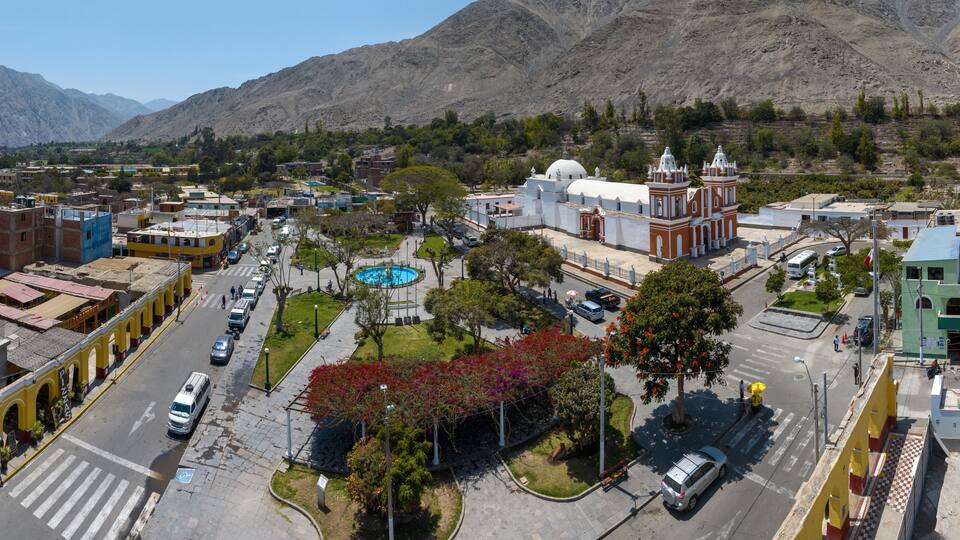 A town with a central plaza, a church, and mountains in the background.