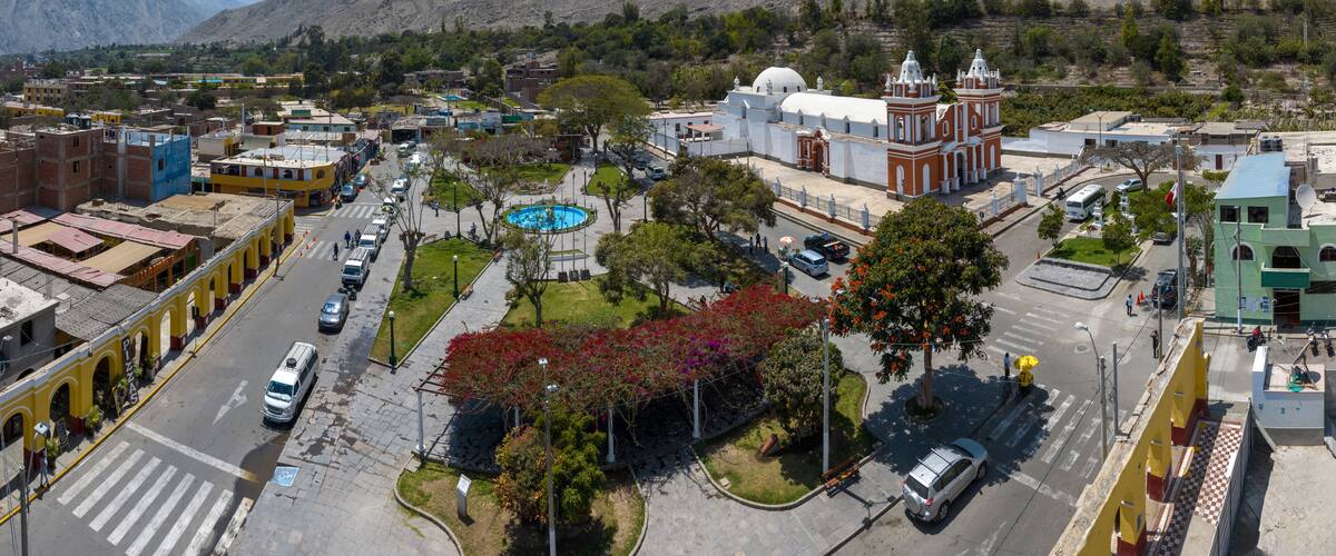 A town with a central plaza, a church, and mountains in the background.