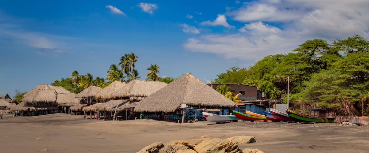 A beach with thatched-roof huts, palm trees, and colorful boats.
