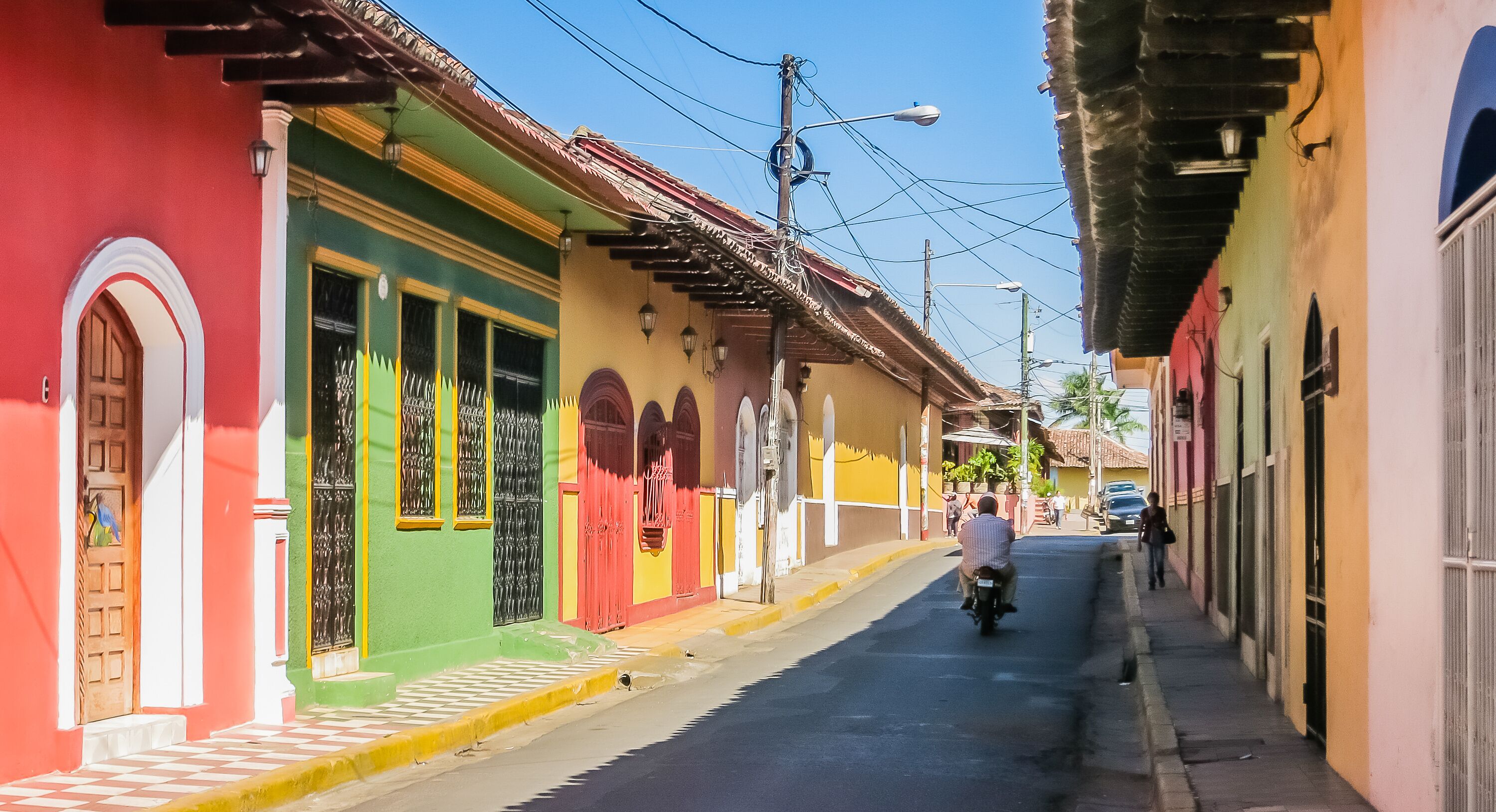 A narrow street lined with colorful buildings, a motorcyclist, and a pedestrian.