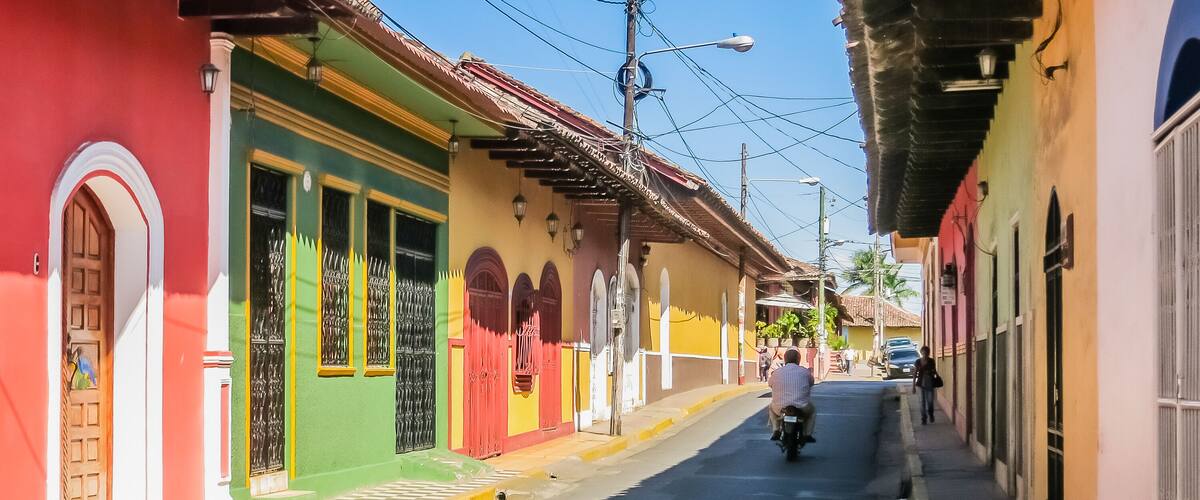 A narrow street lined with colorful buildings, a motorcyclist, and a pedestrian.