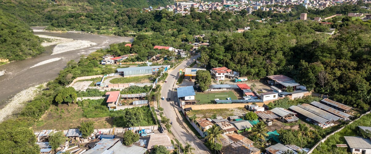 A mountainous landscape with a river, a small town, and a larger city in the background.