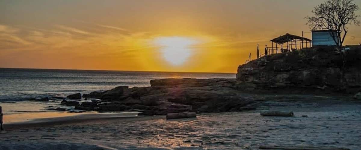 A sunset over a rocky beach with a small structure on the right.