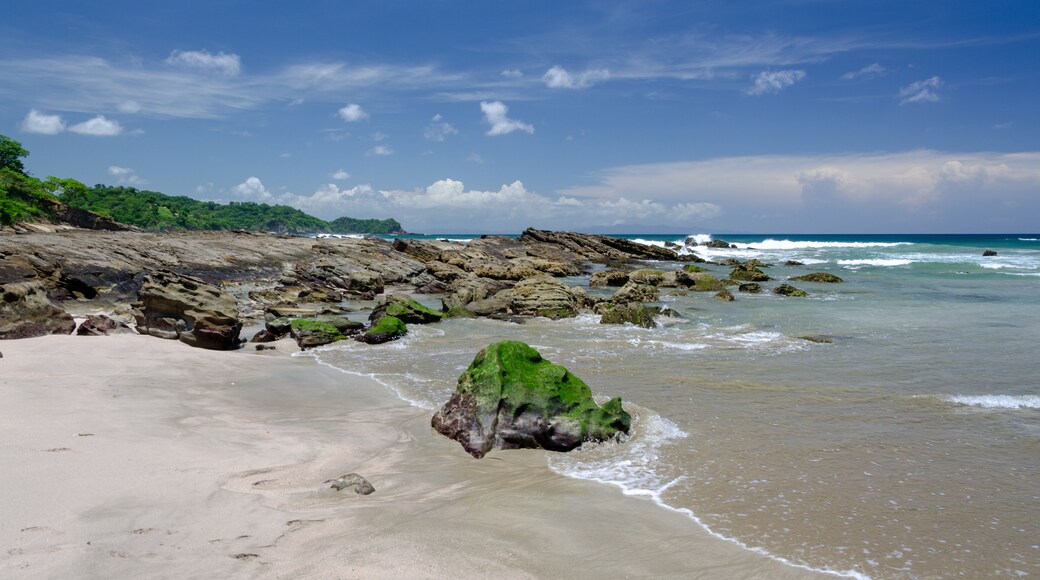 Une plage de sable avec des affleurements rocheux et des vagues qui déferlent sur le rivage.