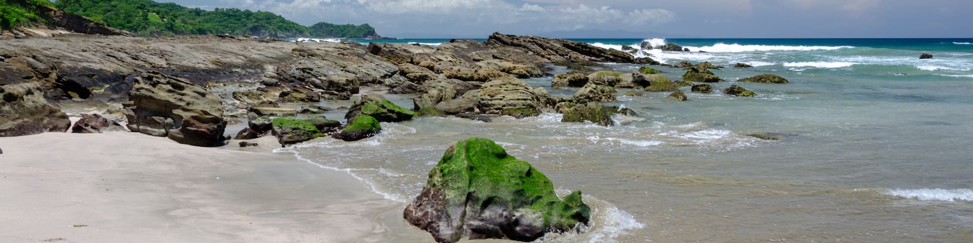 A sandy beach with rocky outcrops and waves crashing onto the shore.