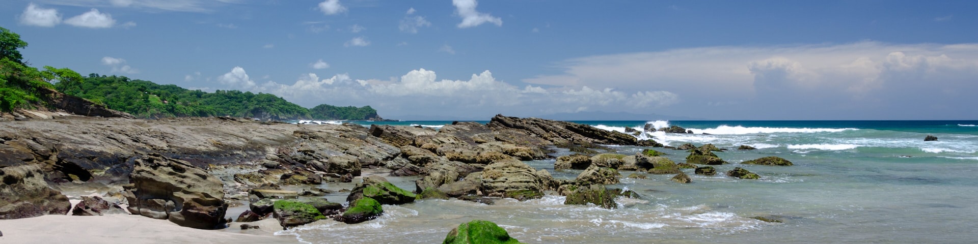 A sandy beach with rocky outcrops and waves crashing onto the shore.